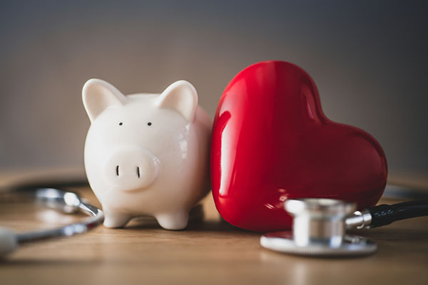 piggy bank next to a doctor stethescope and toy heart