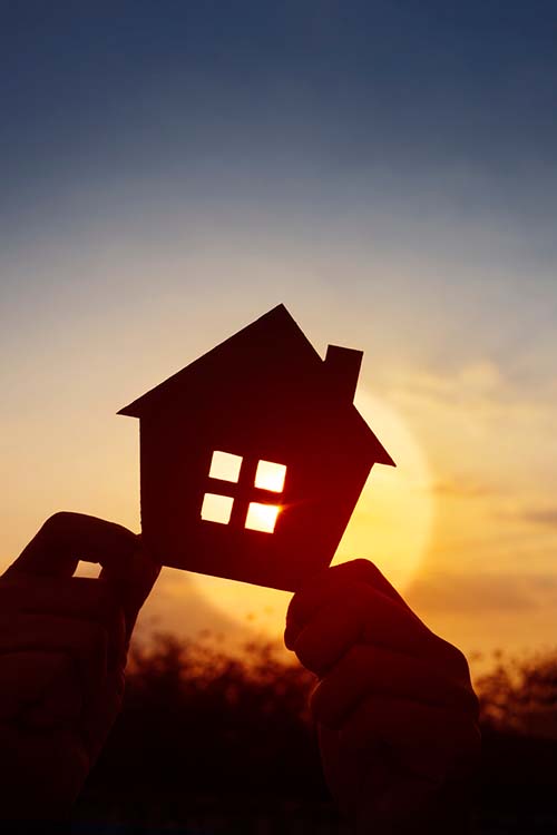 hands holding a silhouette of a house against a sunset