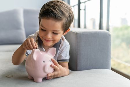 young child putting coins in a piggy bank